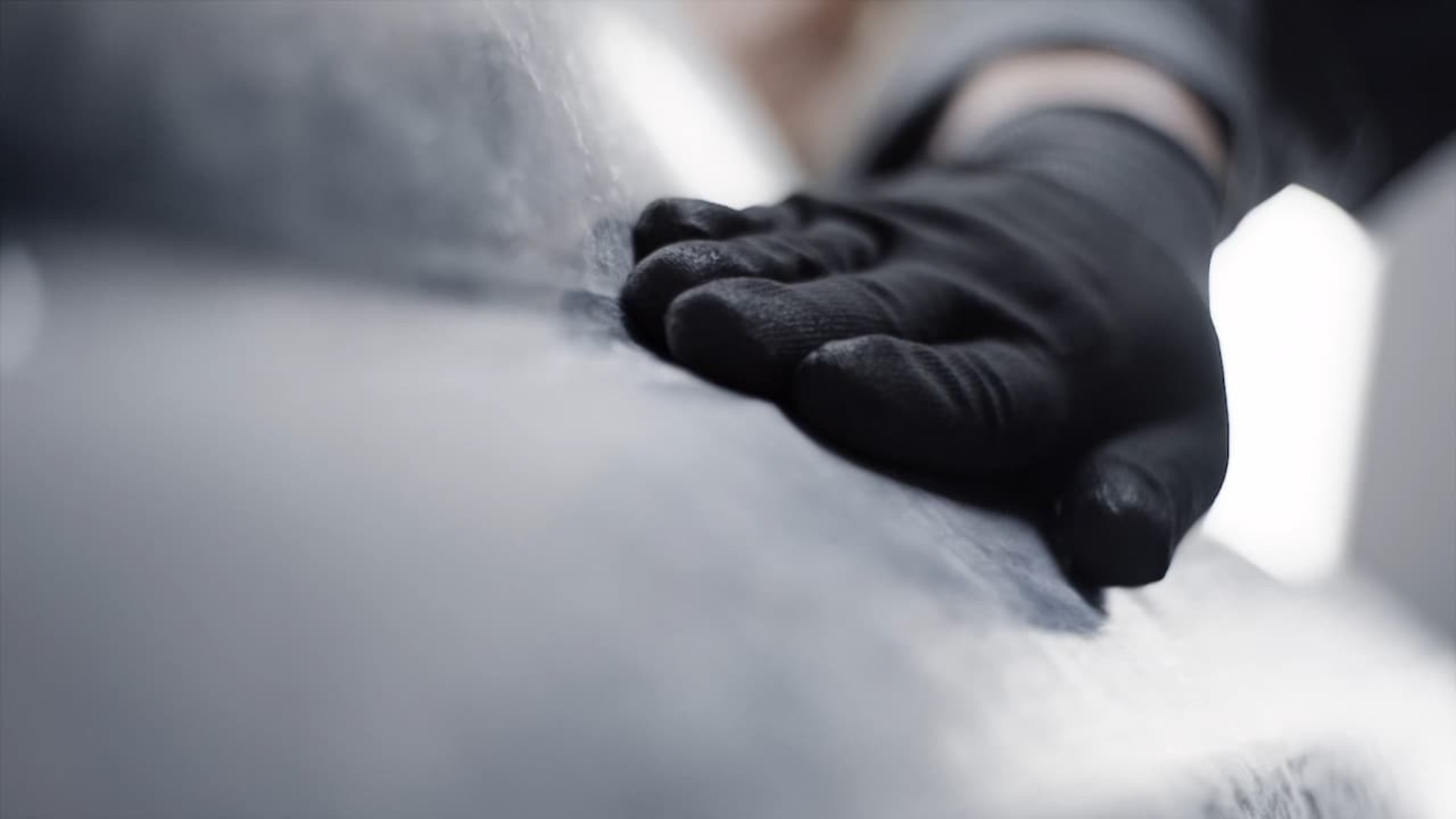 A hand wearing gloves working on a Rolls-Royce car