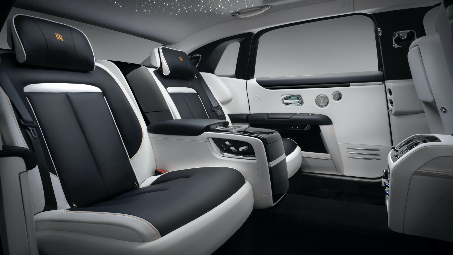 An interior shot of a Rolls-Royce motor car with grey interior including headrests with conform cushions and elegantly embroidered Rolls-Royce logo in orange.,