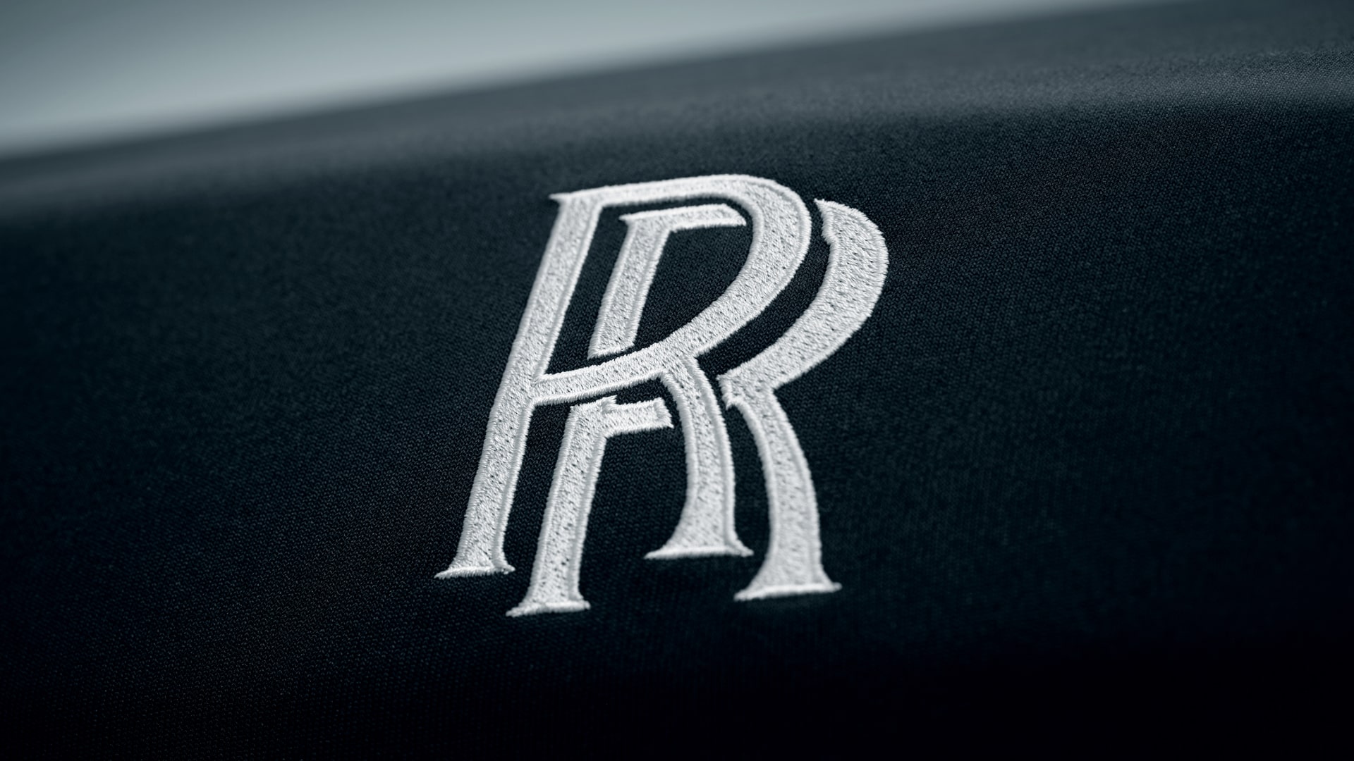 Detailed view of the embroidered RR monogram on the front of the Rolls-Royce car cover in black colour