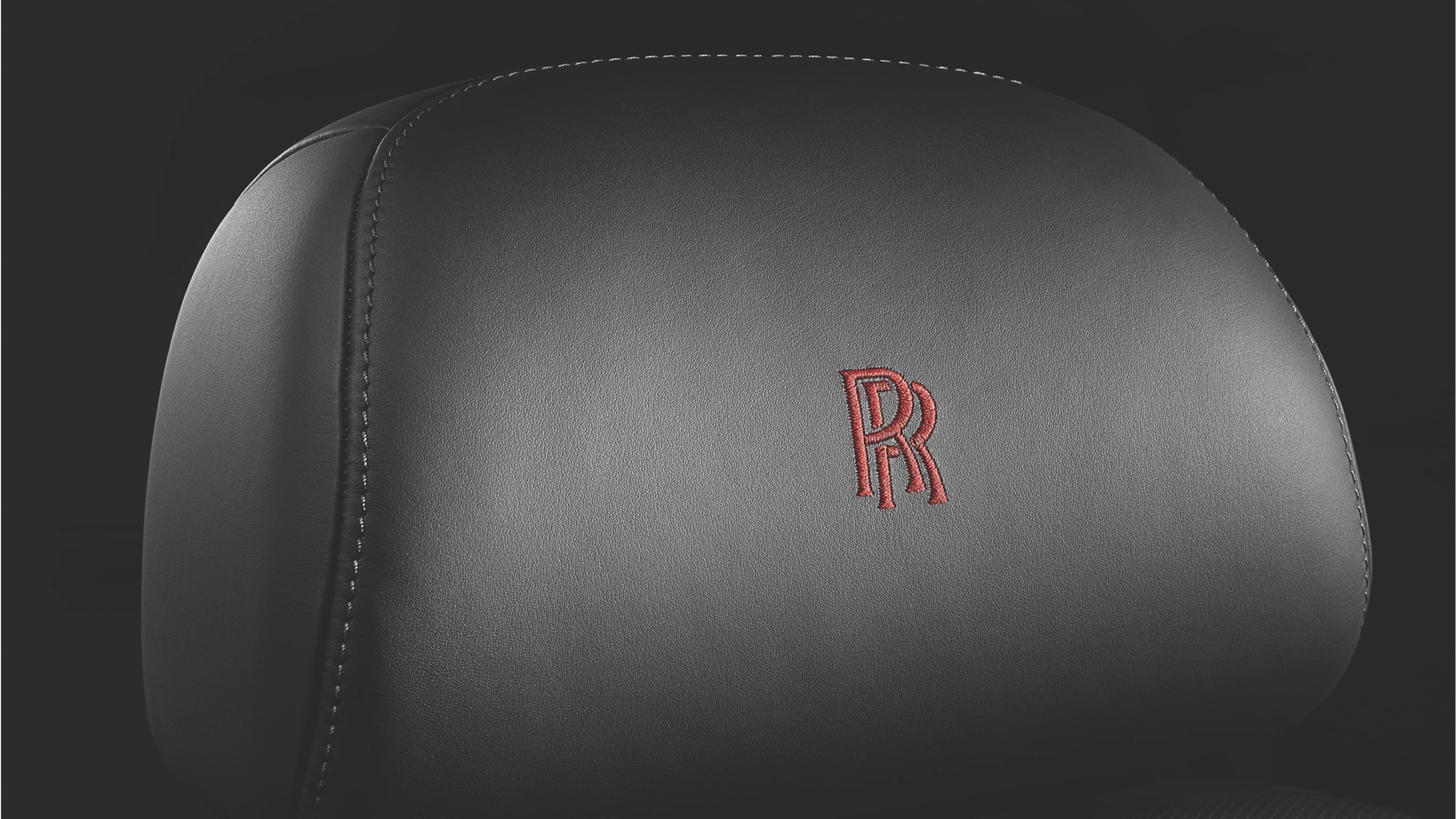Signature red Rolls-Royce monogram embroidered onto leather headrests of a Rolls-Royce motor car