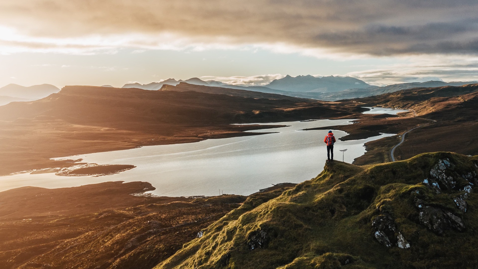 Man looks over stunning, sublime vista of mountains and lake with the Rolls-Royce Pursuit Seat by his side