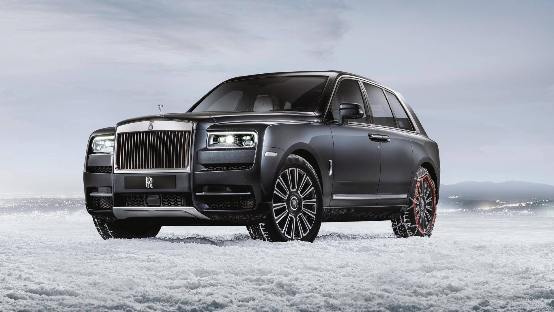 3/4 front exterior of stationary Rolls-Royce Cullinan motor car with snow chains in snowy landscape