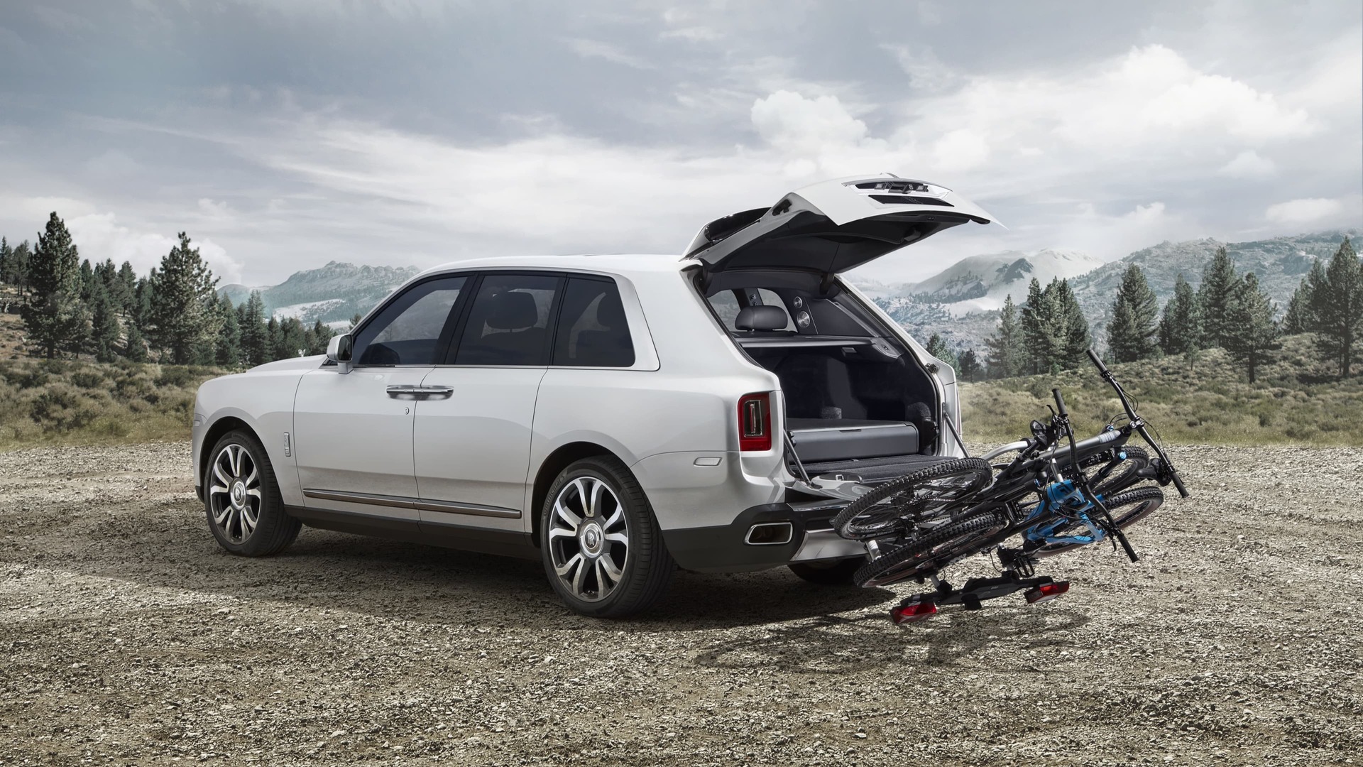 Exterior view of Rolls-Royce Cullinan motor car with trunk open and tow bar mounted bicycle carrier in mountainous landscape