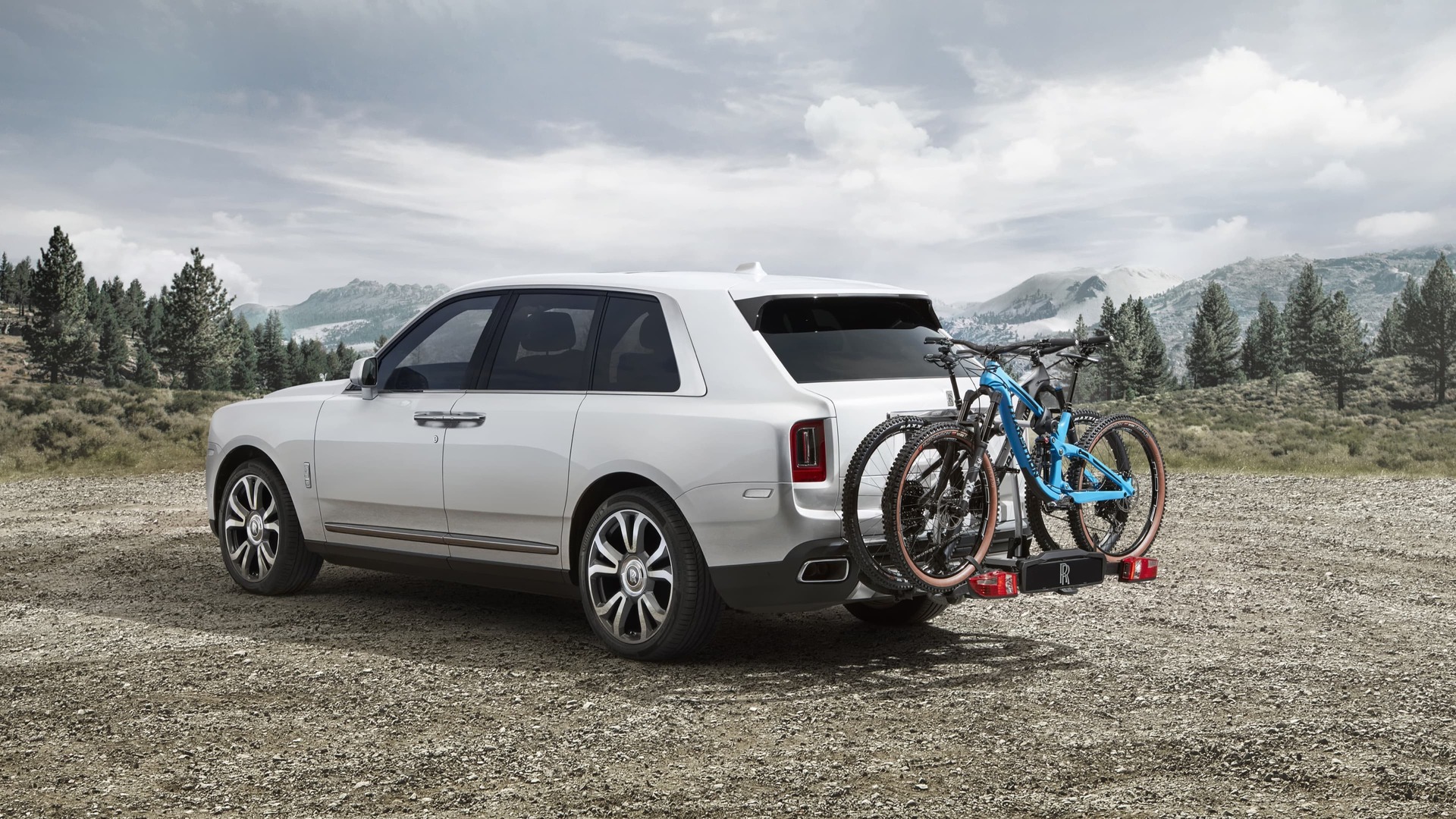 3/4 rear exterior view of Rolls-Royce Cullinan motor car with tow bar mounted bicycle carrier in mountainous landscape