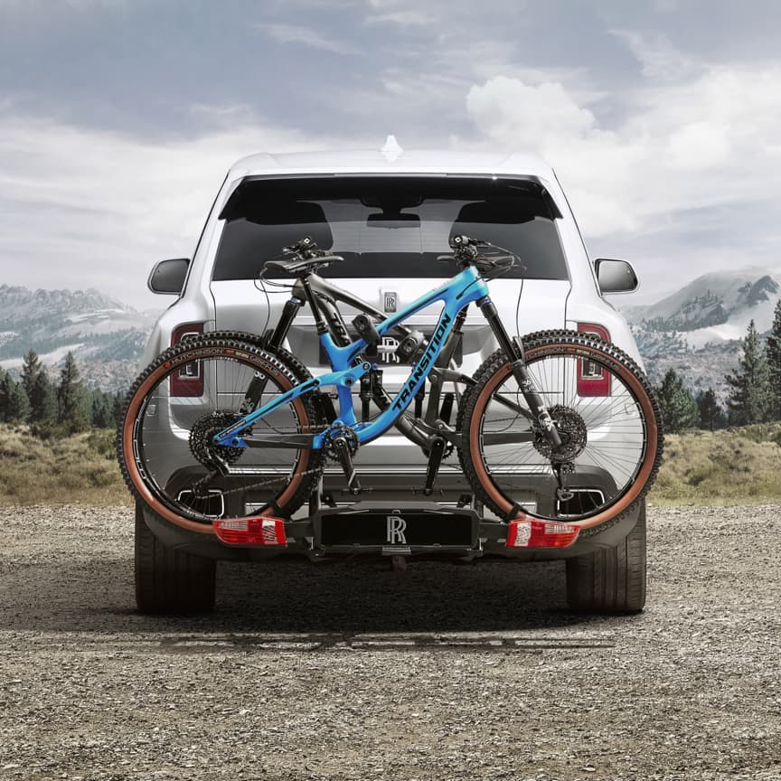 Rear exterior view of Rolls-Royce Cullinan motor car with tow bar mounted bicycle carrier in mountainous landscape