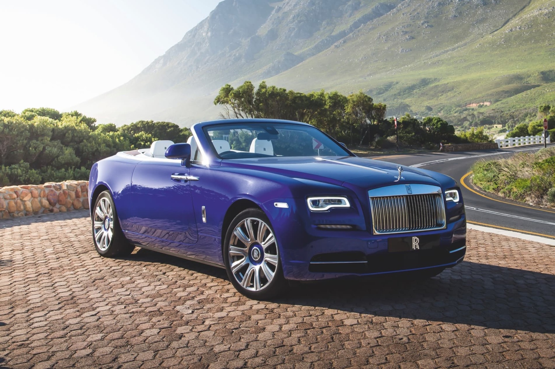 3/4 front exterior of stationary drophead coupé Rolls-Royce Dawn motor car with green, mountainous background