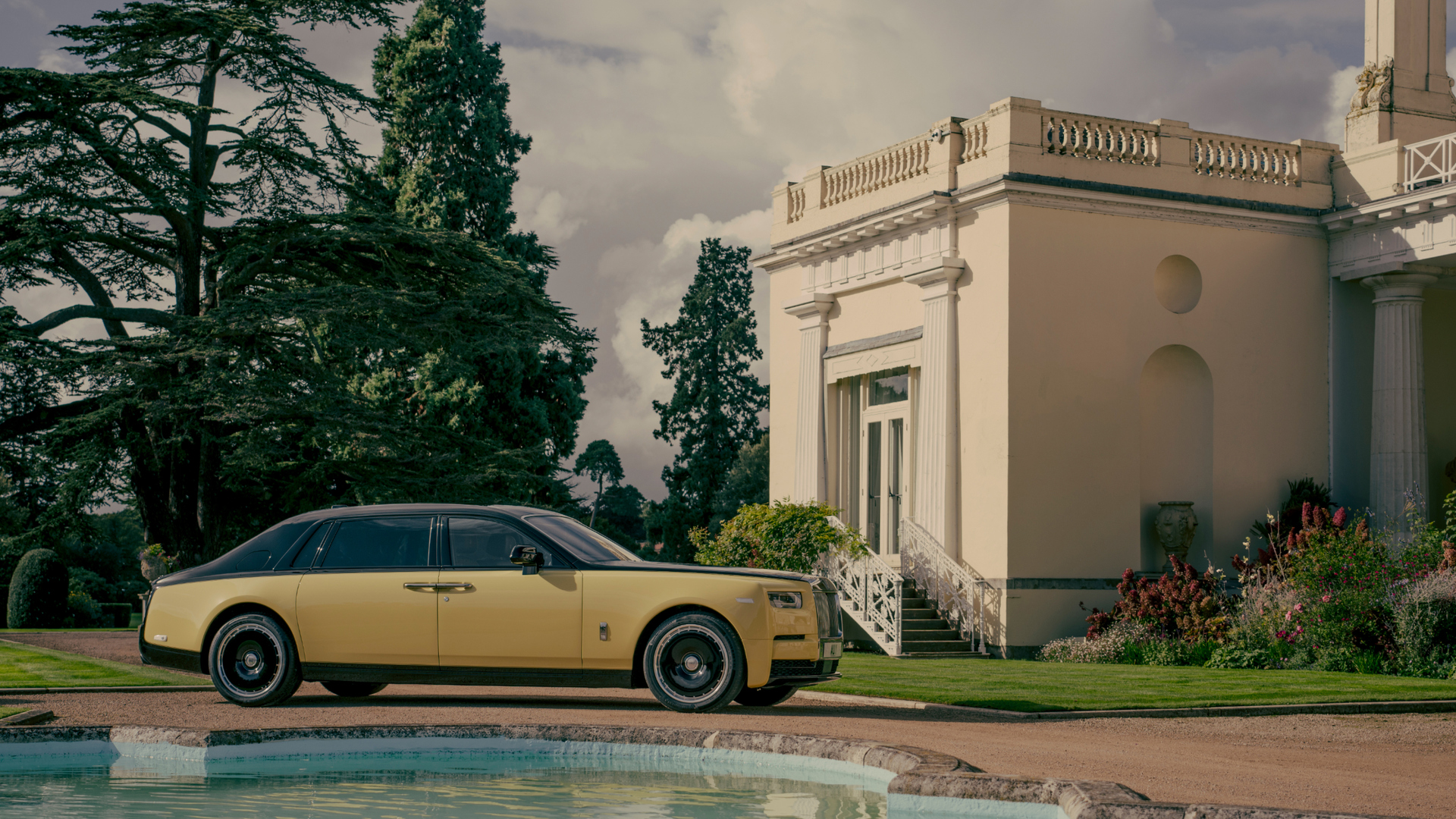 Horizontal shot of the Phantom Goldfinger parked next to a stone fountain. Cream mansion in the background.
